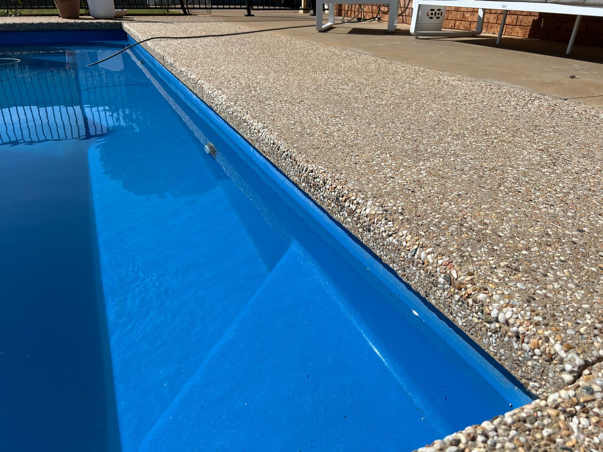 Blue swimming pool with steps, next to a textured, tan deck.