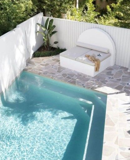 Small pool with steps, white walls, and a built-in daybed. Turquoise water, flagstone patio, and lush greenery.