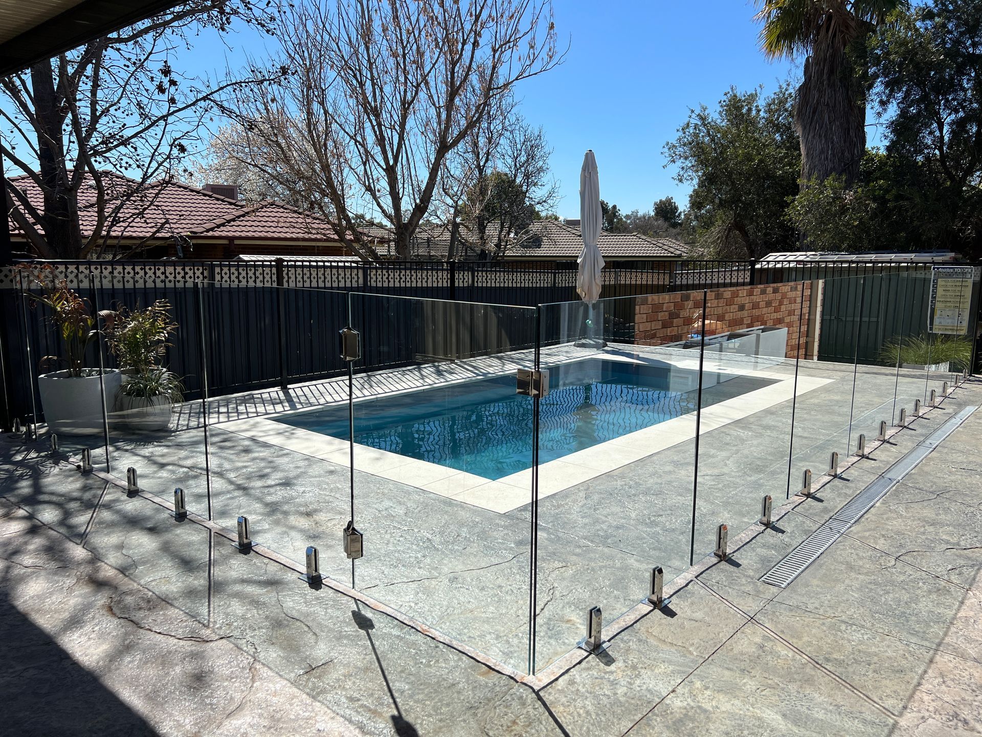 Swimming pool with glass fence on a sunny day. Grey patio, blue water.
