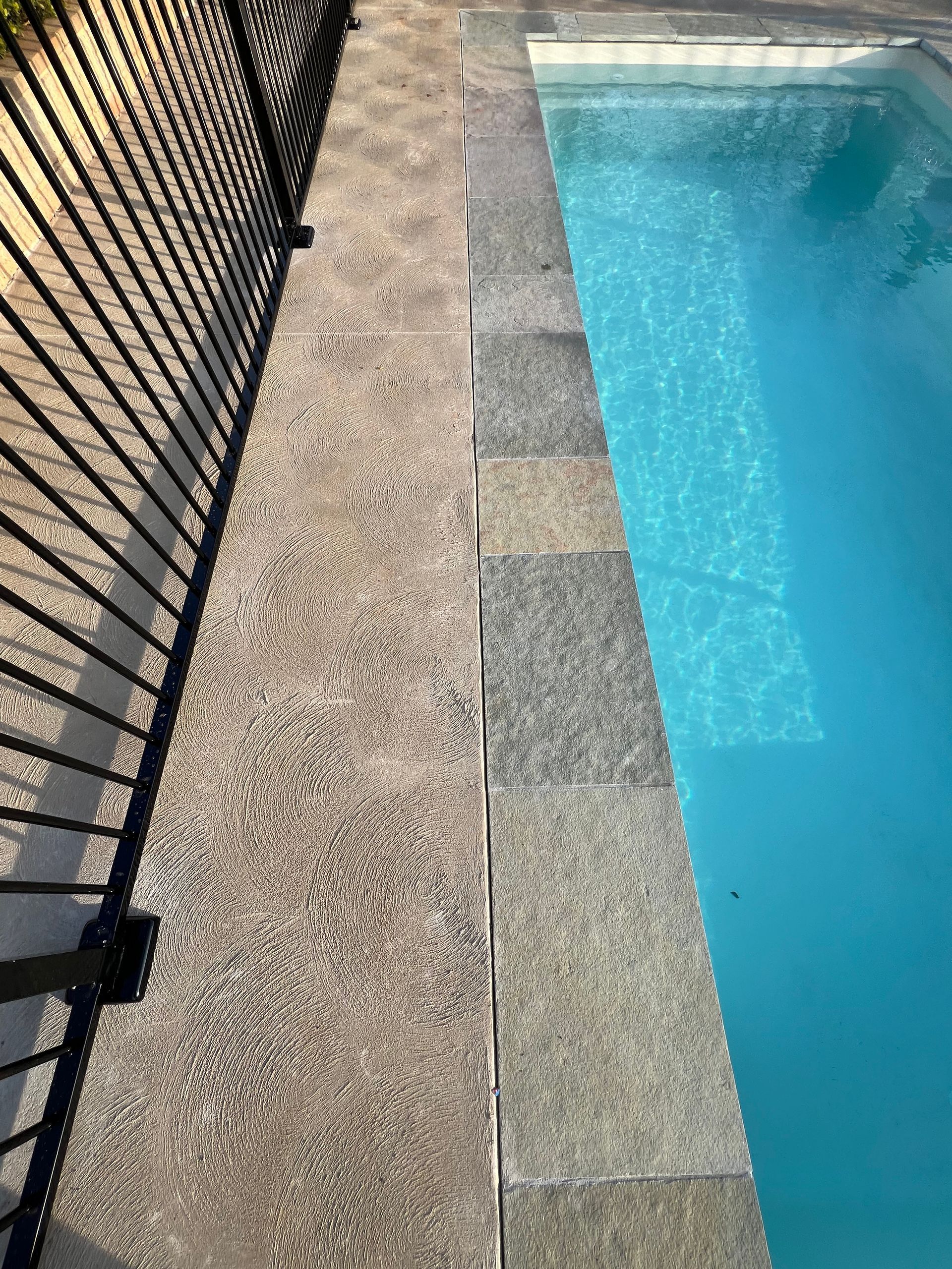 The side of a pool with bright blue water and paving — SJ Pools and Concreting in Bourke, NSW