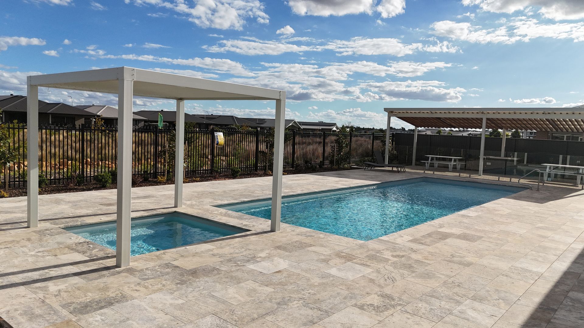 Pool area with two pools, a spa, and pergolas under a blue sky.