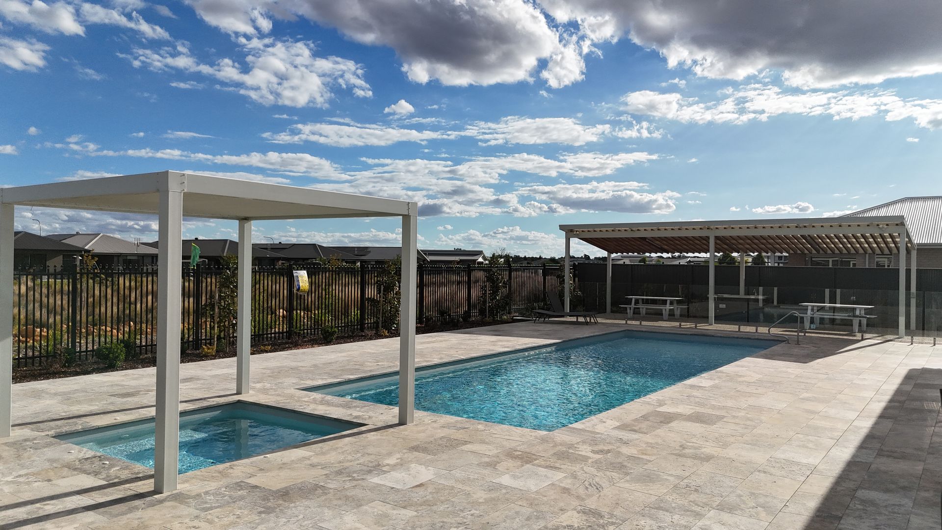 A Medium Swimming Pool Surrounded by a pergola with a black fence — SJ Pools and Concreting in Dubbo, NSW