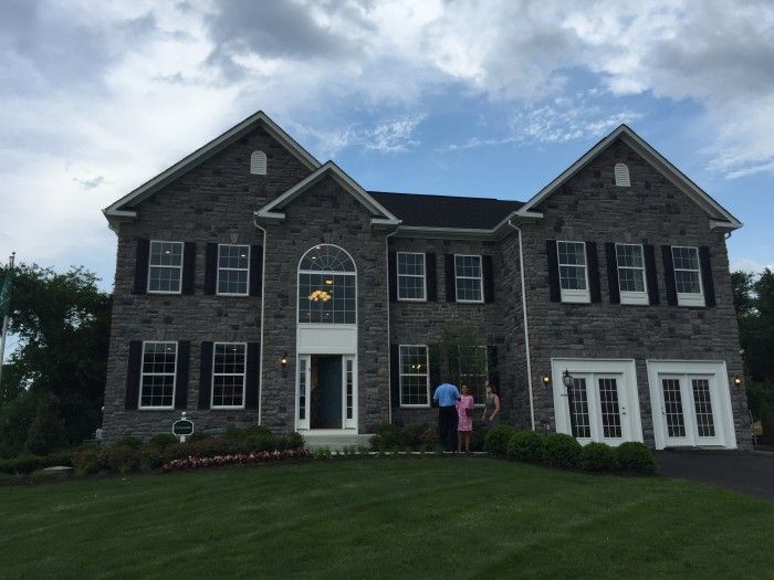 Two-story gray stone house with black shutters, white trim, and a family standing in front.