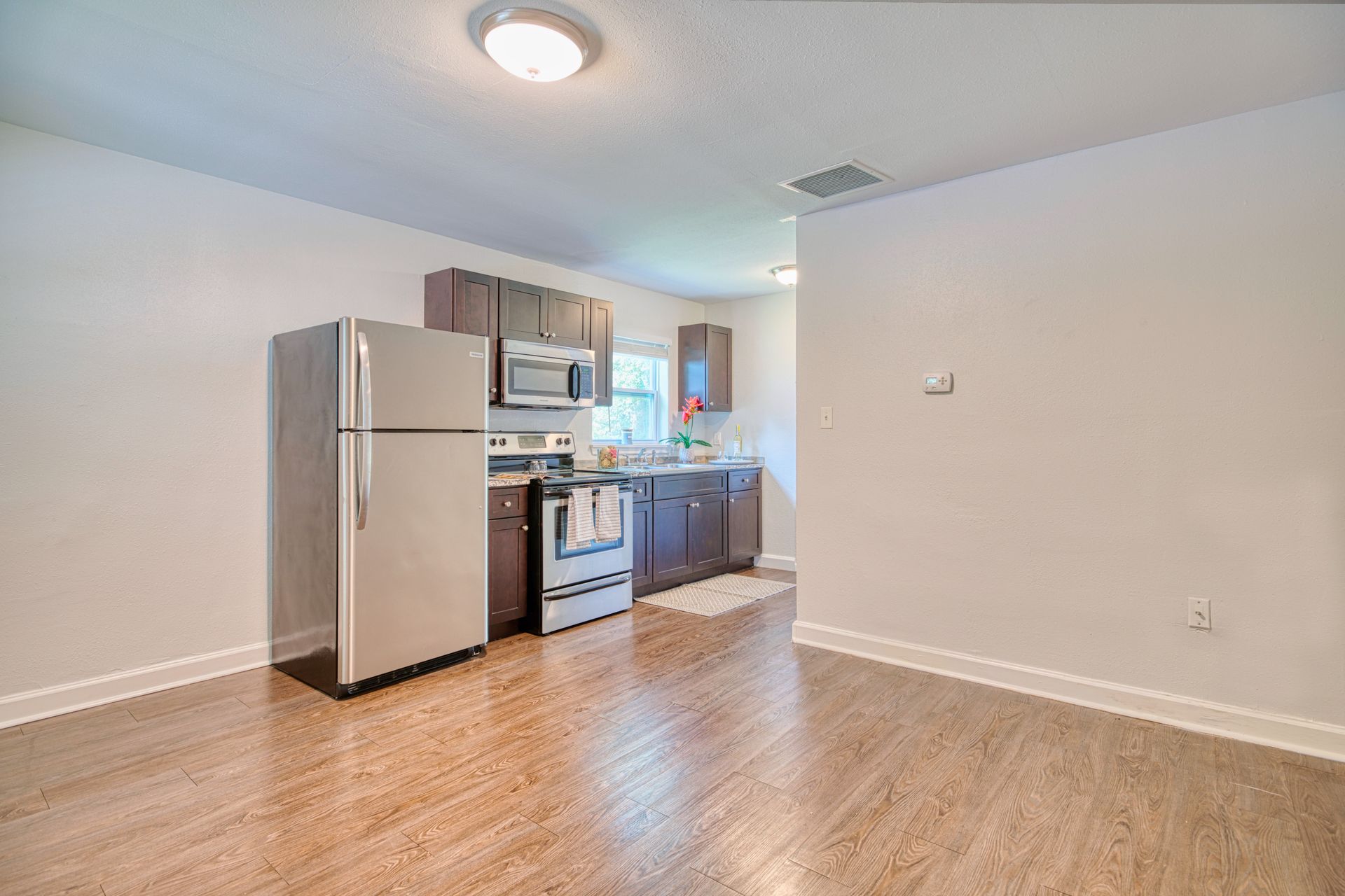 An empty kitchen with a refrigerator , stove , microwave and sink.