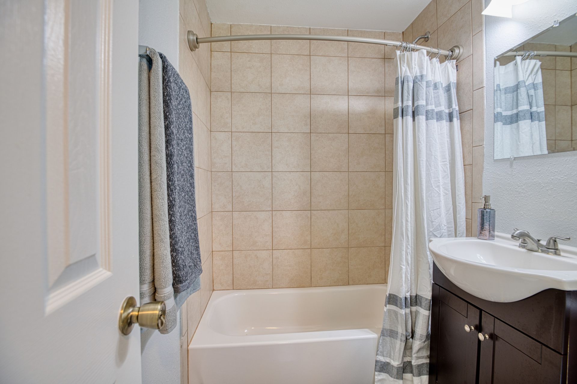 A bathroom with a tub , sink , mirror and shower curtain.
