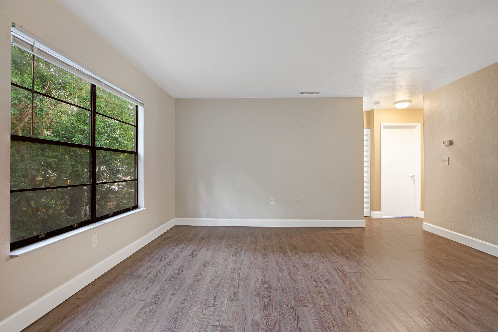 An empty living room with hardwood floors and a large window.