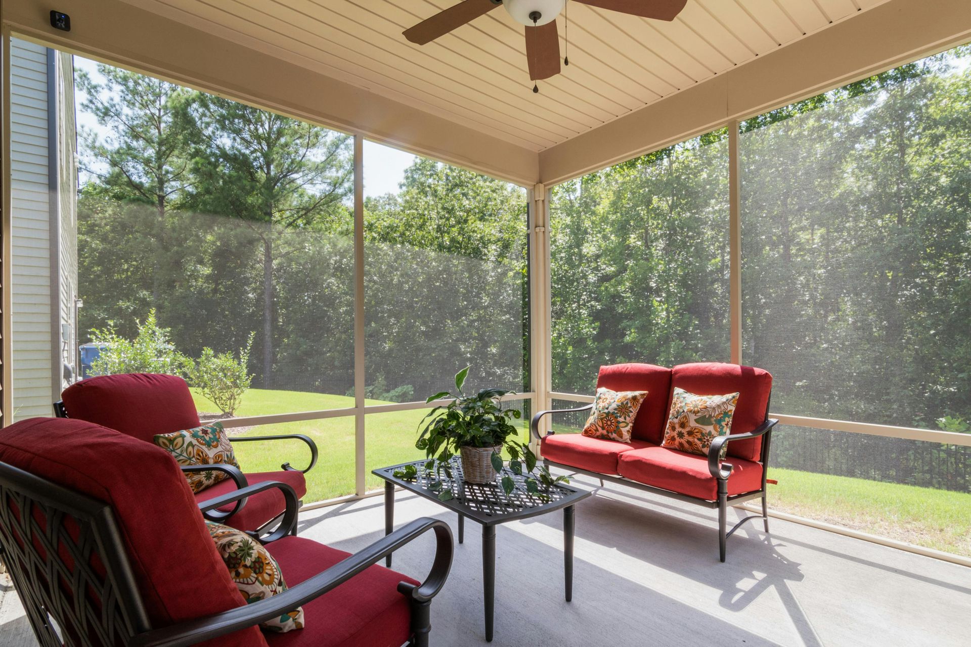 Screened porch with red chairs and sofa around a glass table, overlooking a sunny green yard.