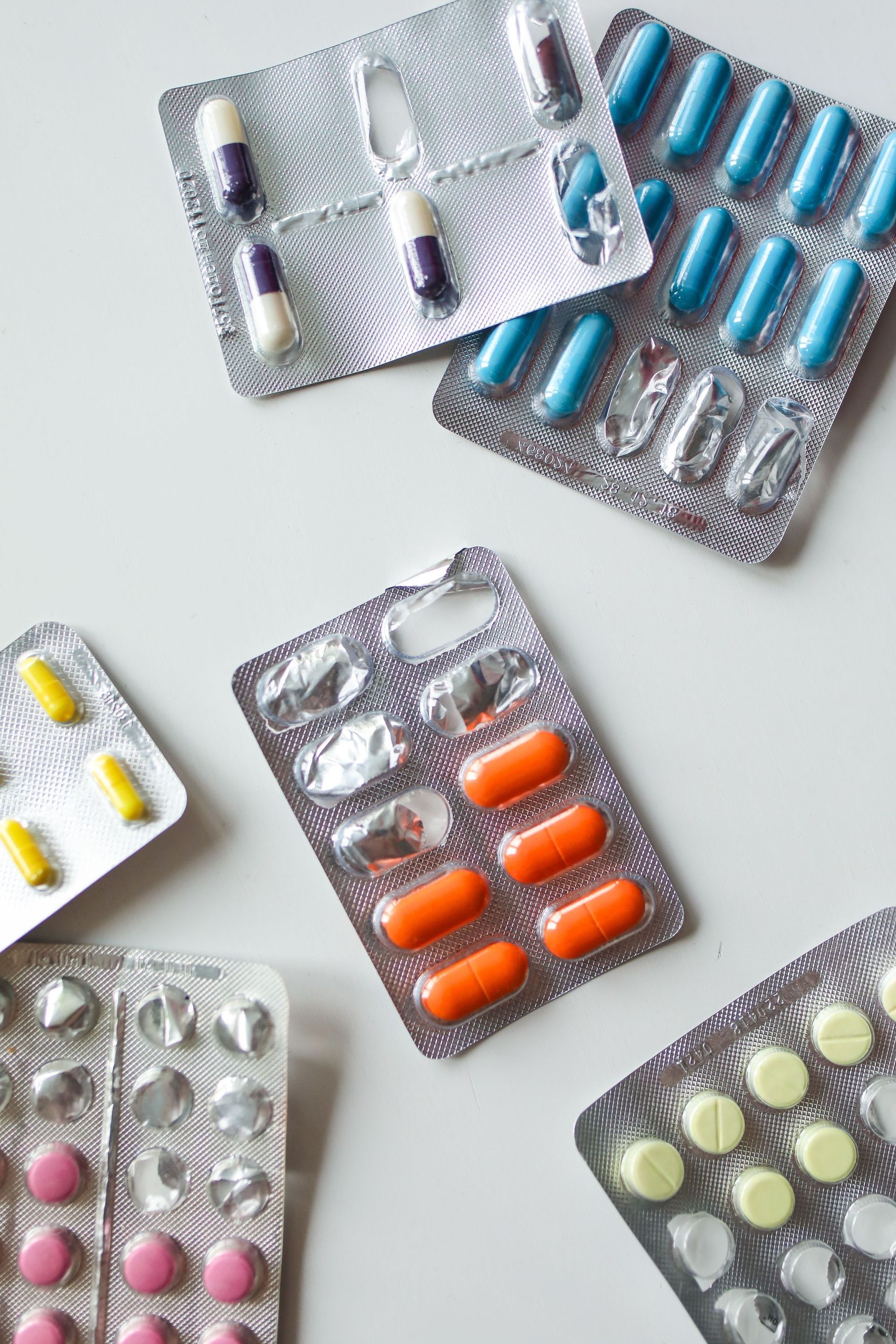 Mehrere Blisterpackungen mit Tabletten und Kapseln in verschiedenen Farben auf hellem Untergrund
