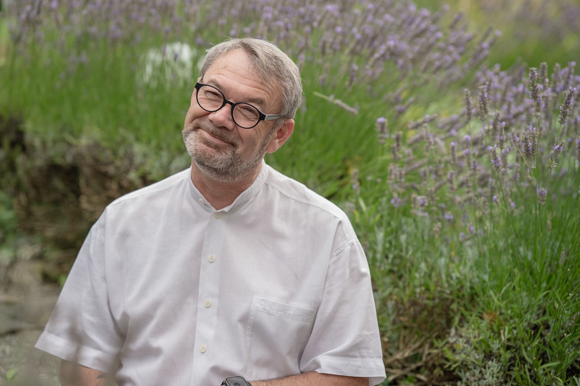 Ein Mann mit Bart und Brille steht vor einem Lavendelfeld.