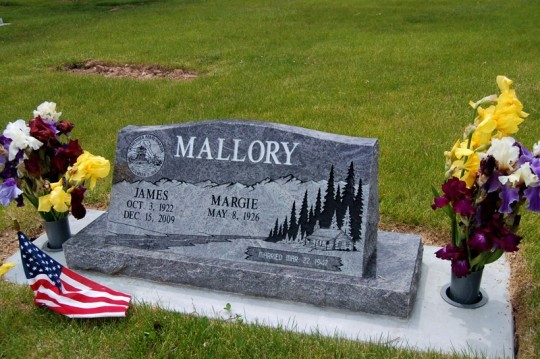 Gray headstone with Mallory name and names/dates, flanked by flowers and flag.