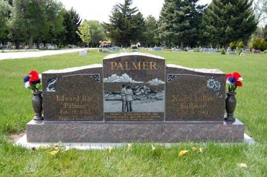 Headstone engraved with name and names, dates, and a photo of a couple. Red, white and blue flowers flank the tombstone.