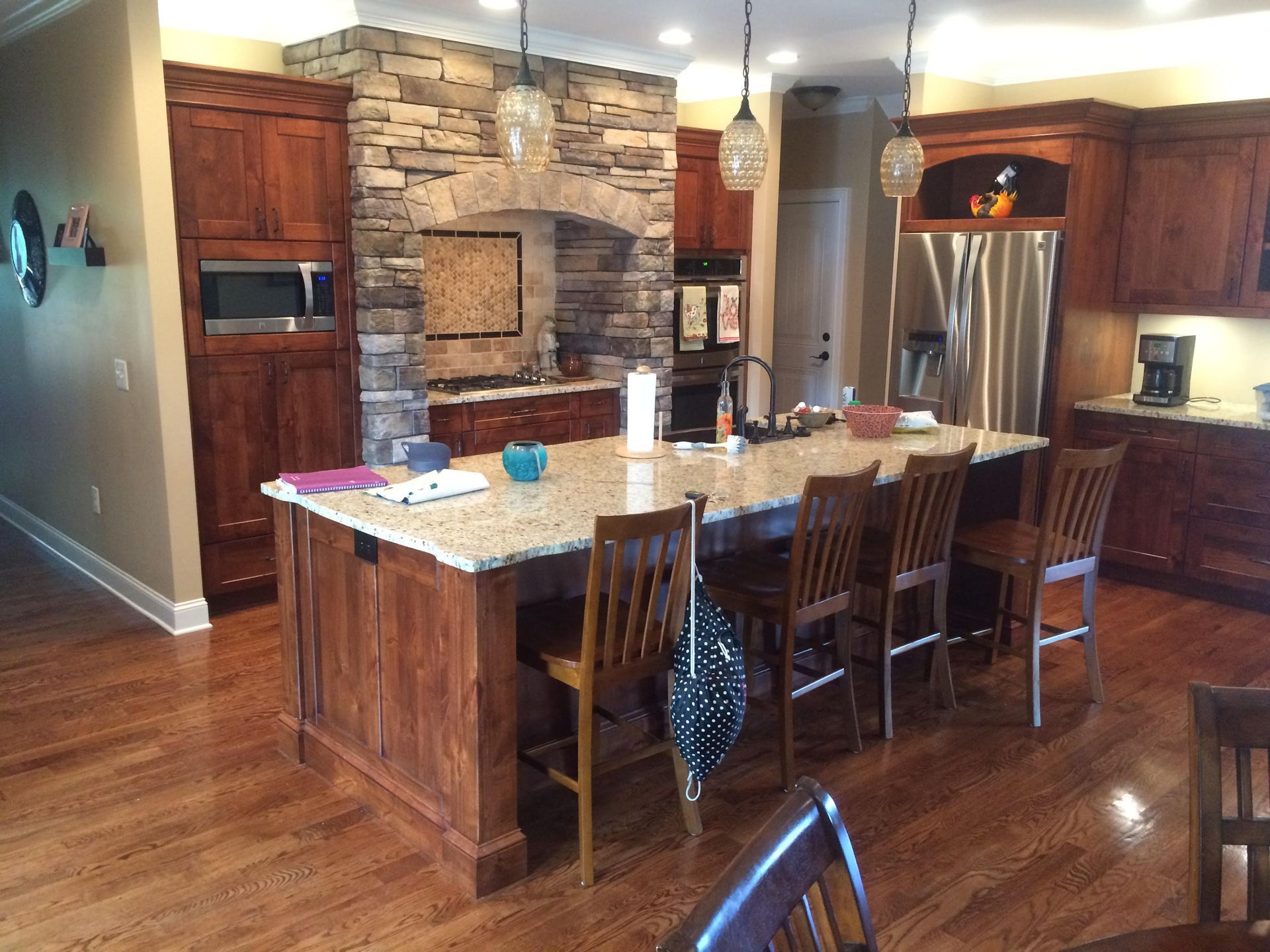 Spacious kitchen with stone island, wood cabinets, stainless fridge, and hardwood floors