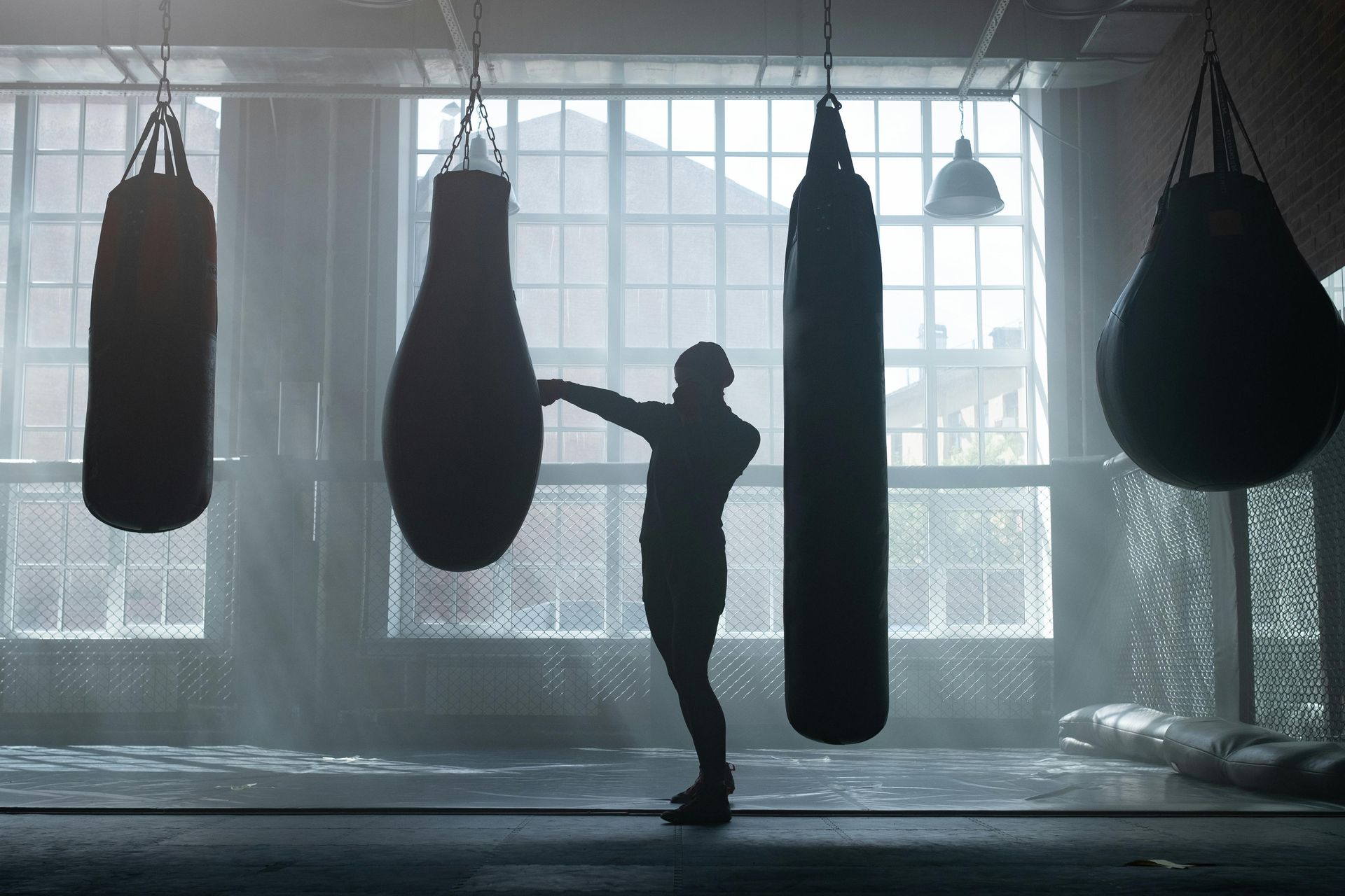 Boxer shadowboxing in a gym with heavy bags, natural light streaming through windows.