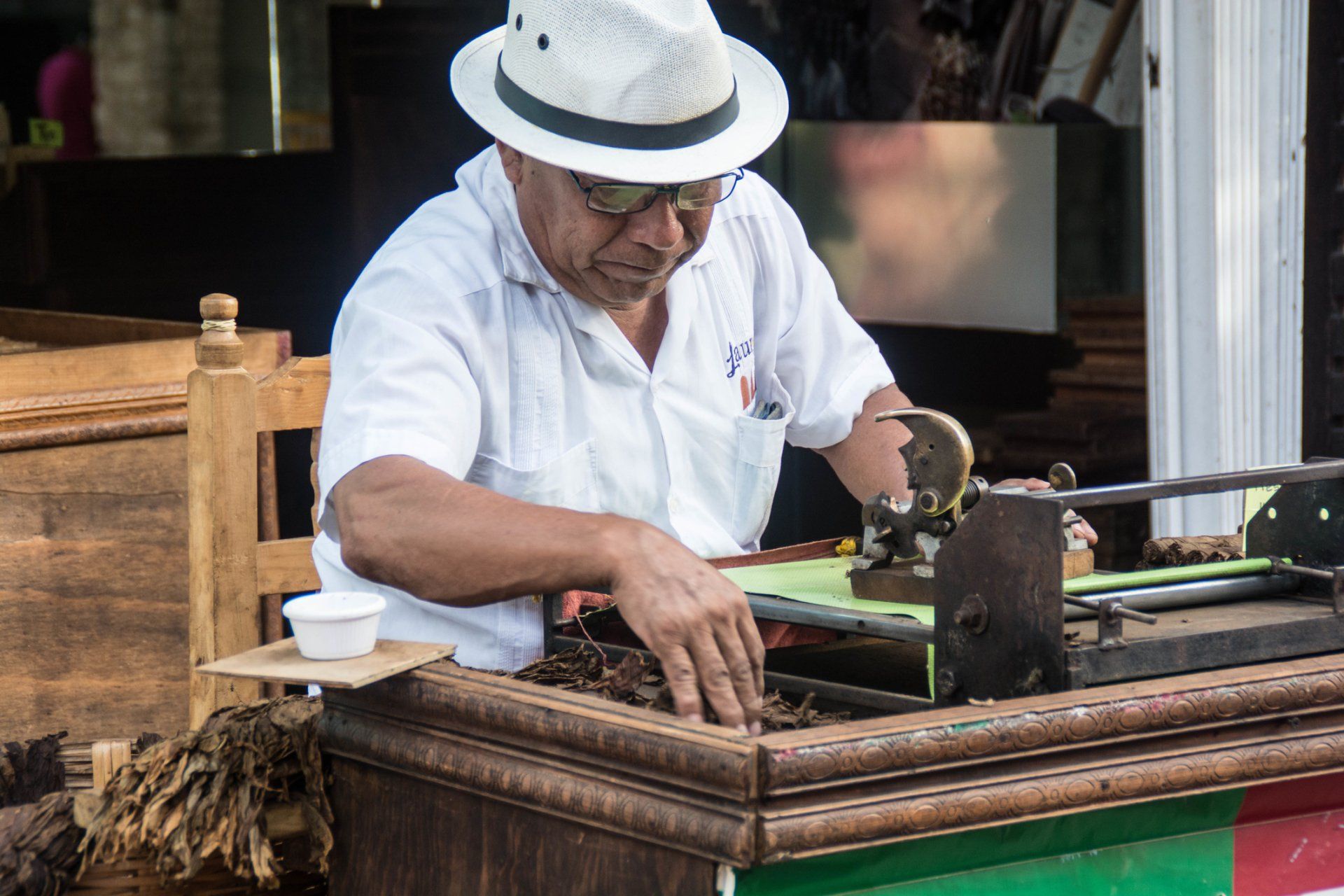 A man in a hat is making cigars on a machine.