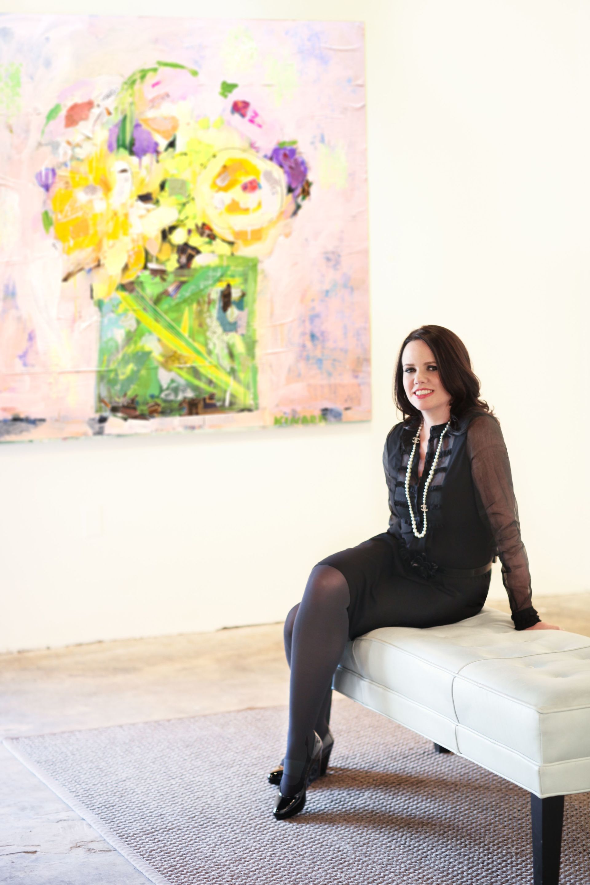 A woman is sitting on a bench in front of a painting of flowers.