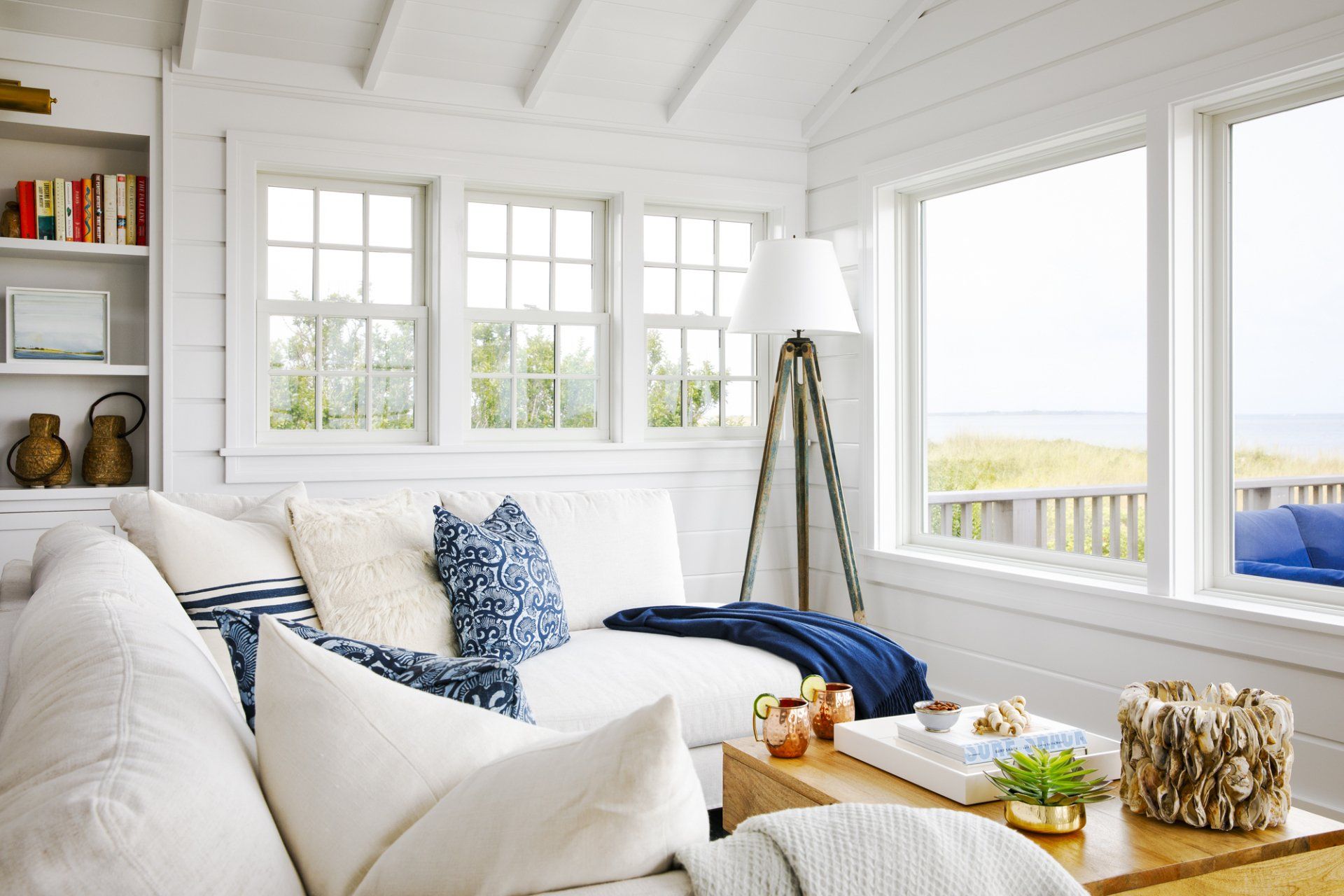 A living room with a couch , table , lamp and lots of windows.