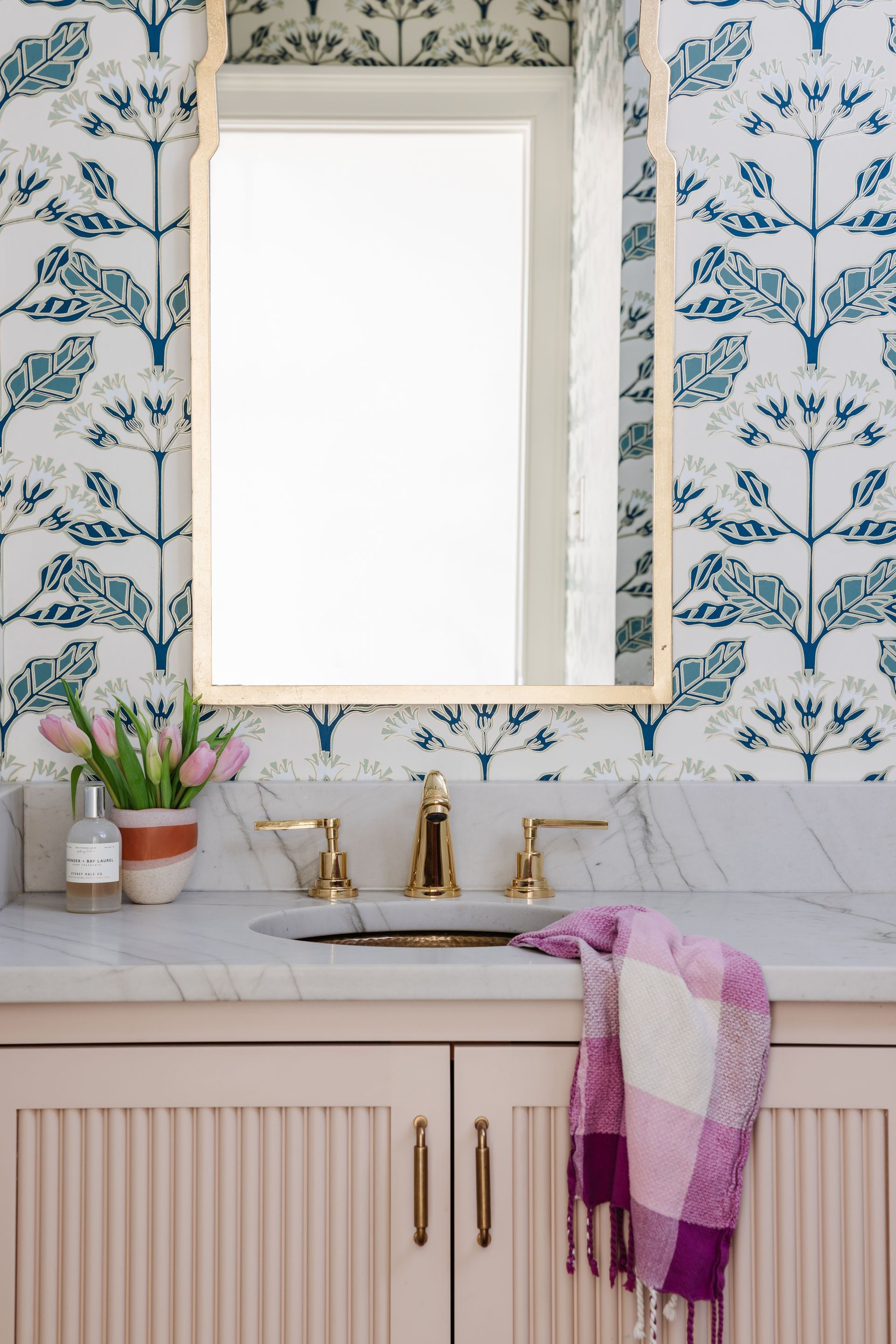 A bathroom with a sink , mirror , and pink cabinets.