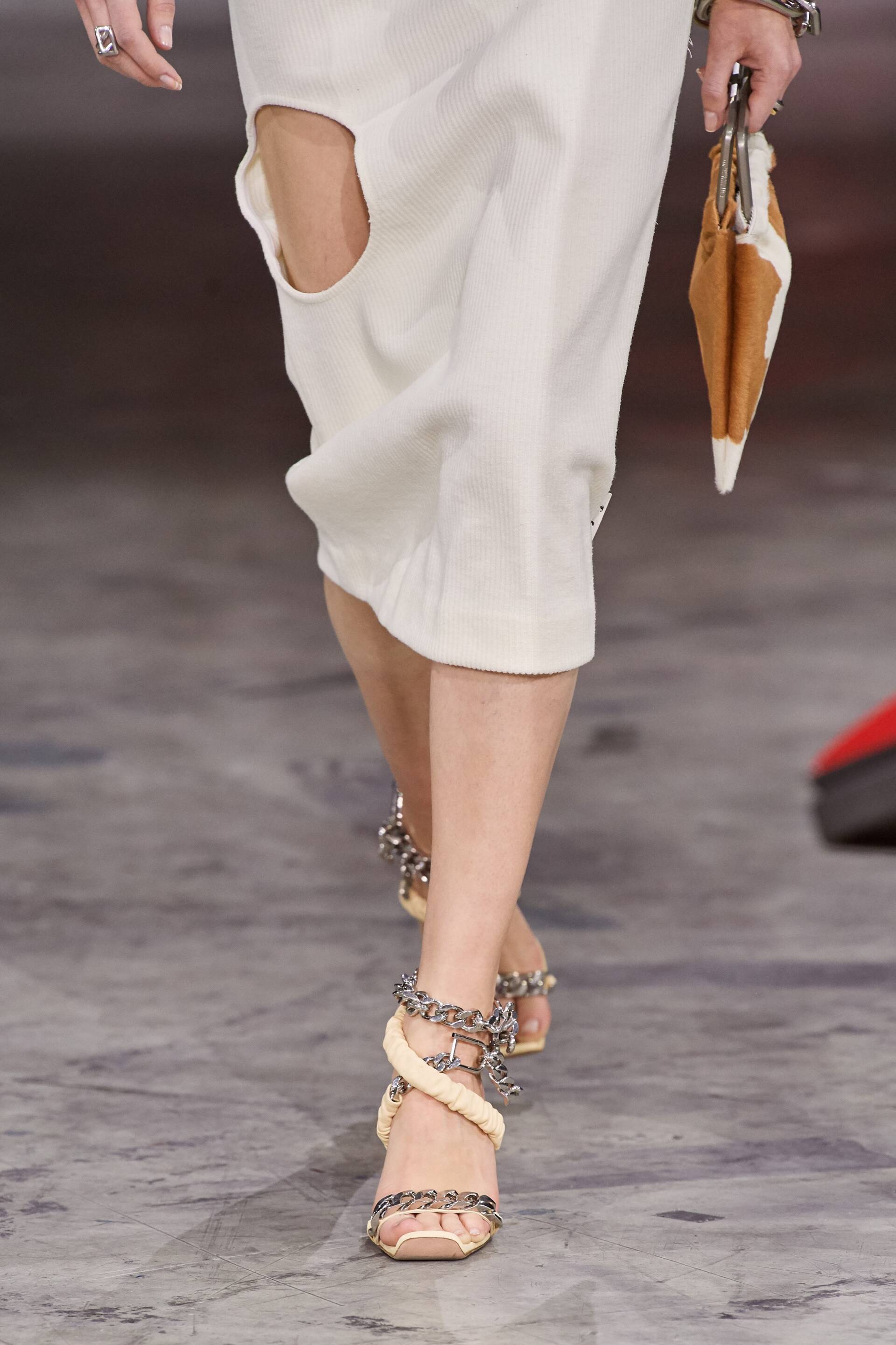 A woman wearing a white dress and sandals is walking down a runway