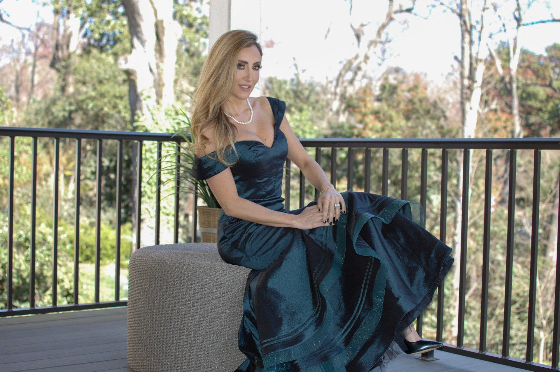 A woman in a long green dress is sitting on a bench on a balcony.