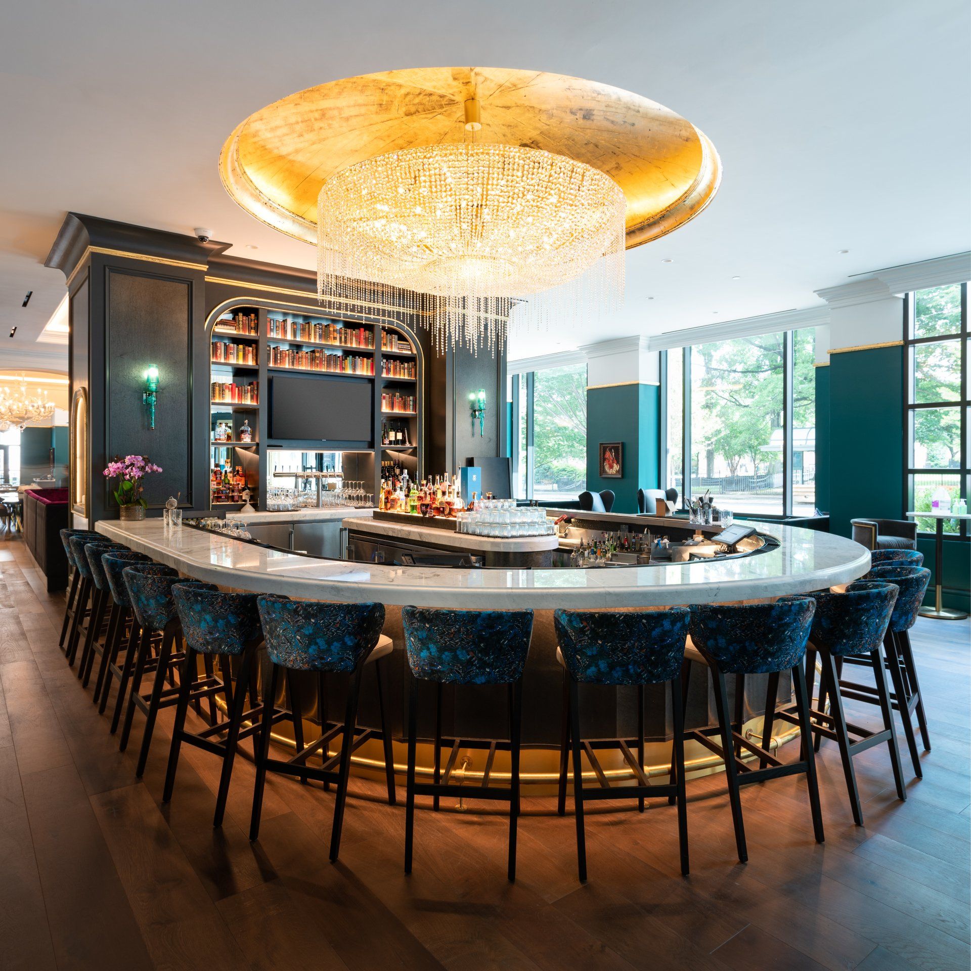 A restaurant with a long bar and stools and a large chandelier hanging from the ceiling.