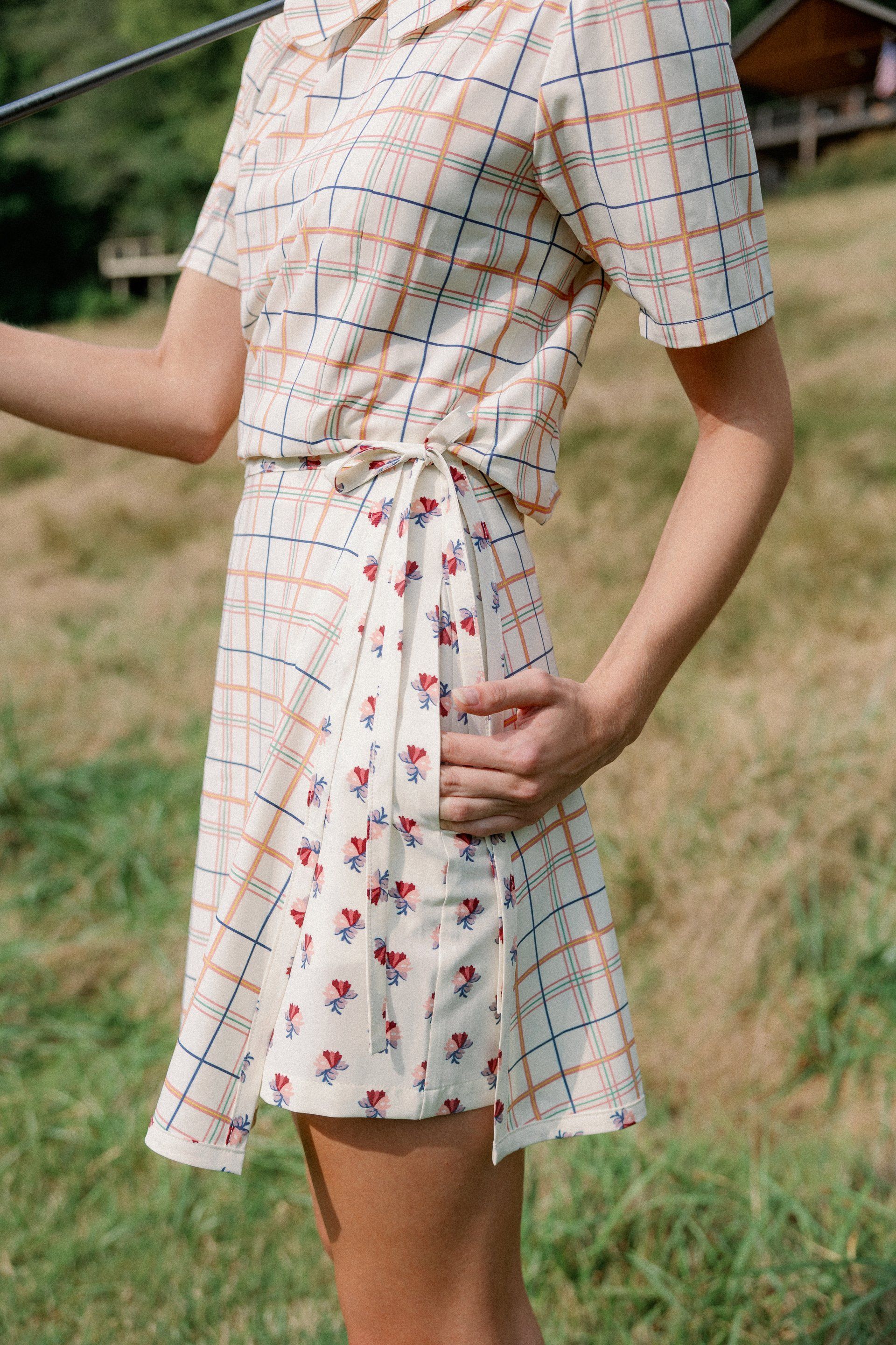 A woman in a plaid dress is standing in a field holding a golf club.