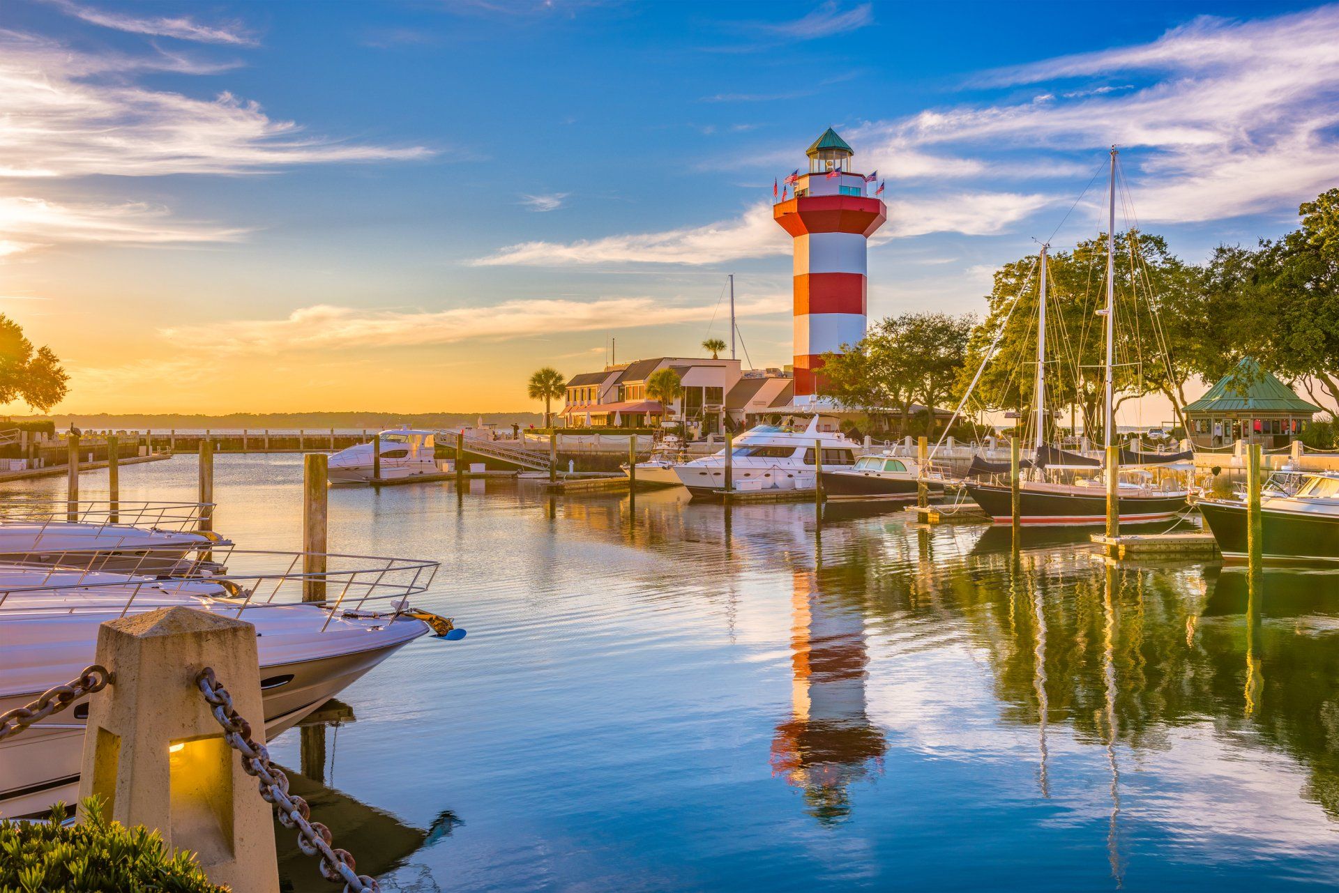 A red and white lighthouse is sitting in the middle of a harbor surrounded by boats.