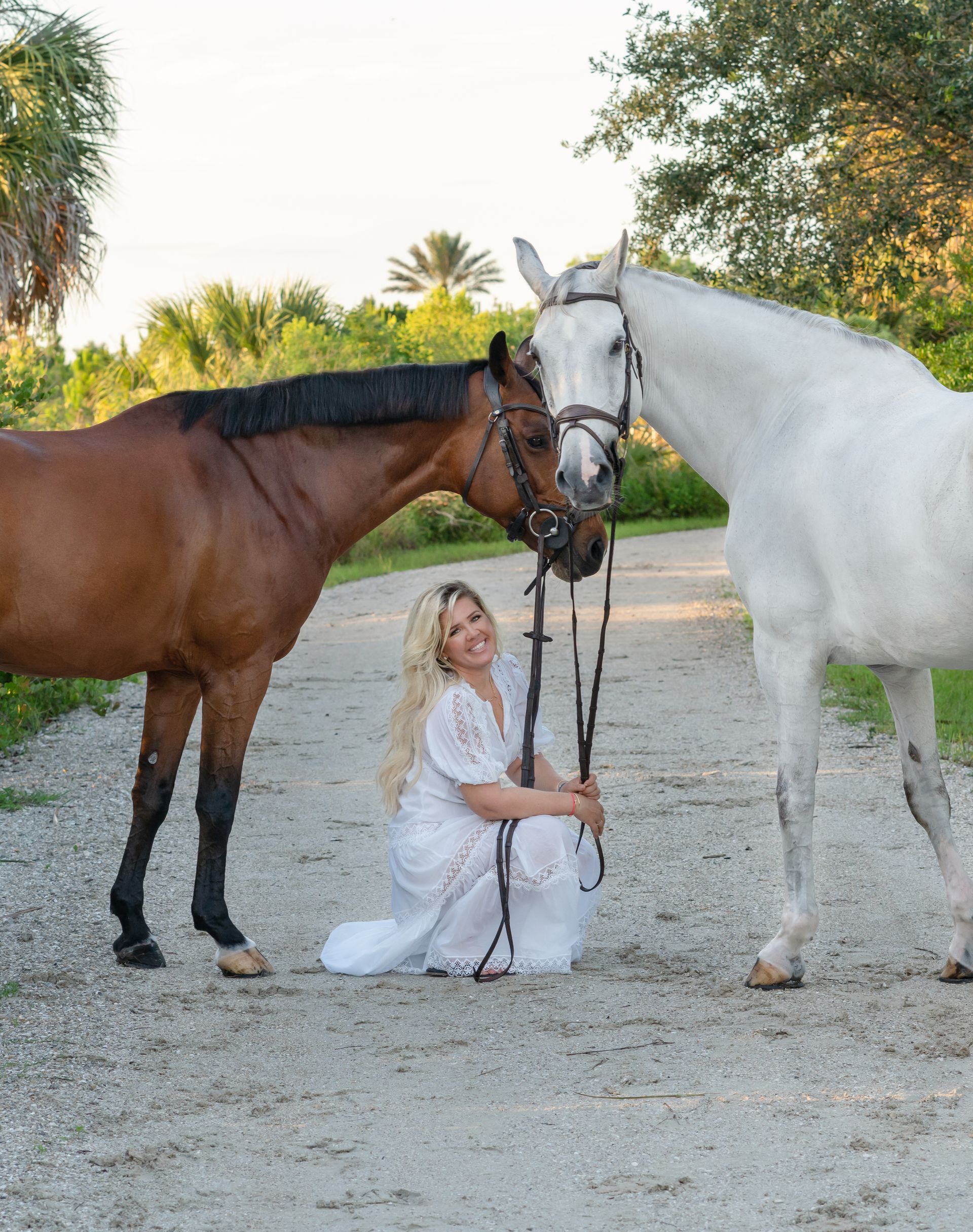 A woman in a white dress is kneeling next to two horses.