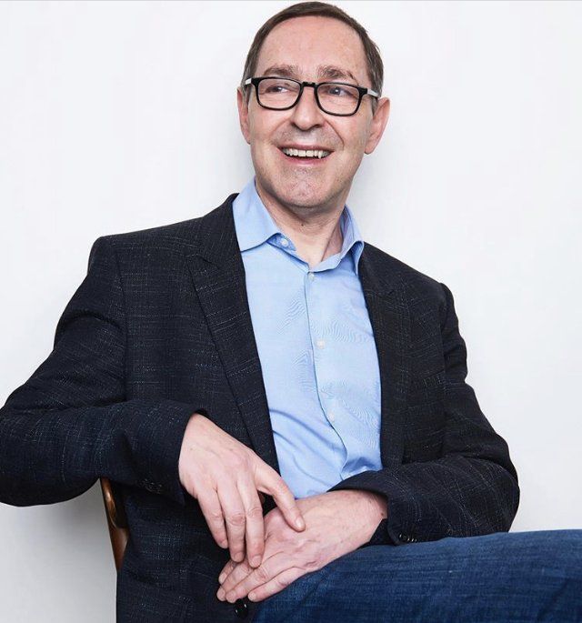 A man wearing glasses and a suit is sitting in a chair