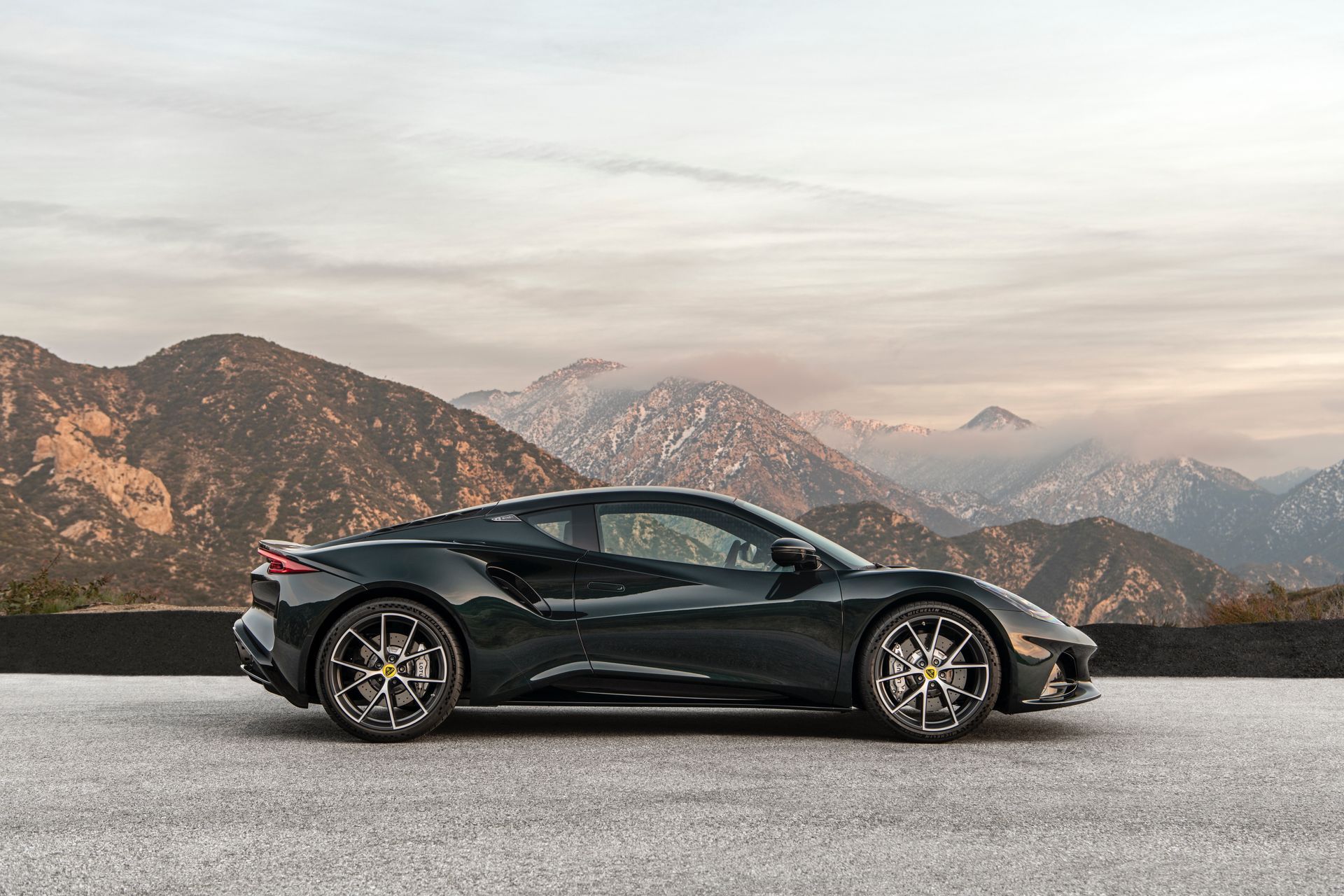 A black sports car is parked on the side of a road with mountains in the background.