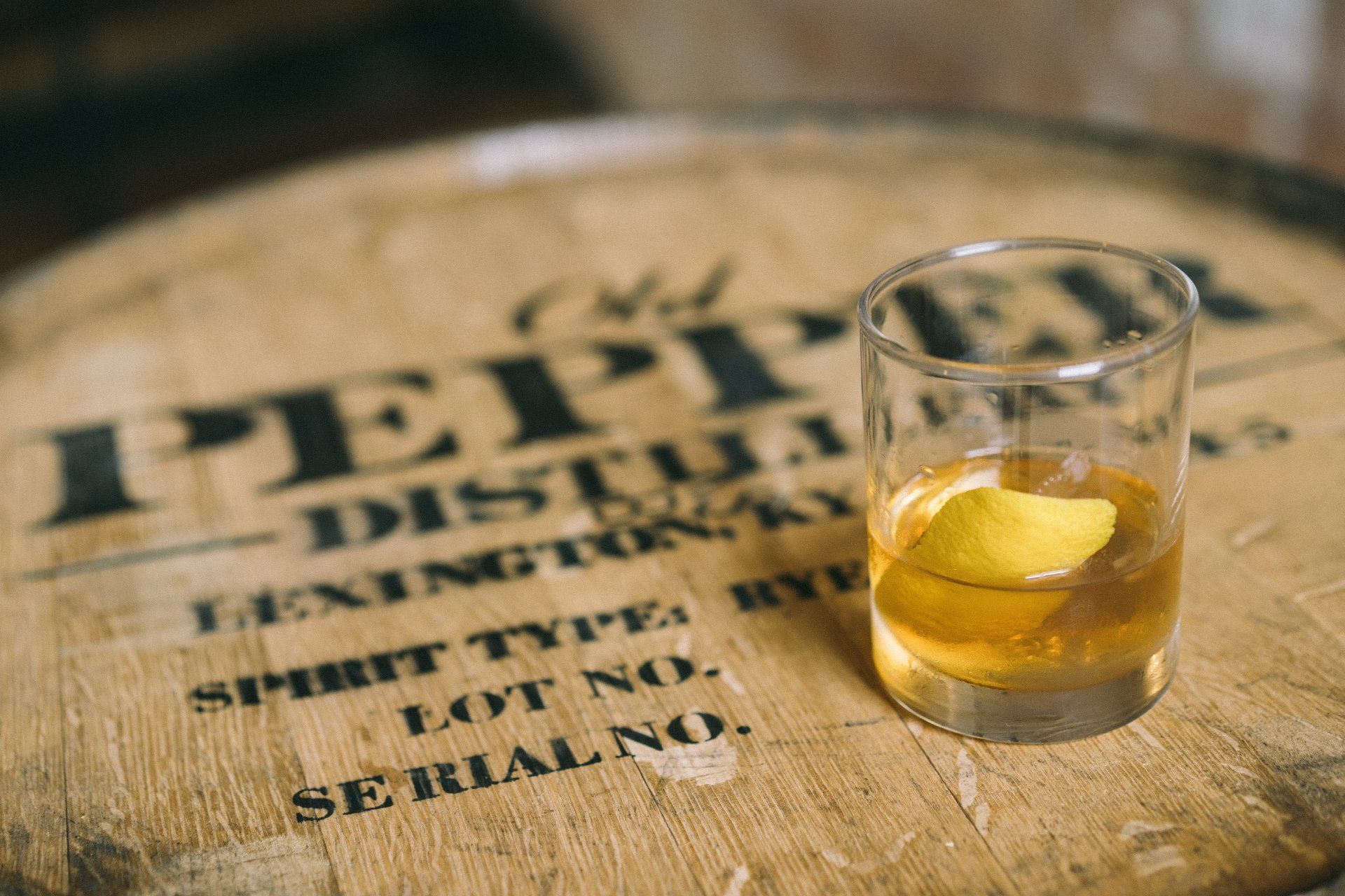 A glass of whiskey is sitting on top of a wooden barrel.
