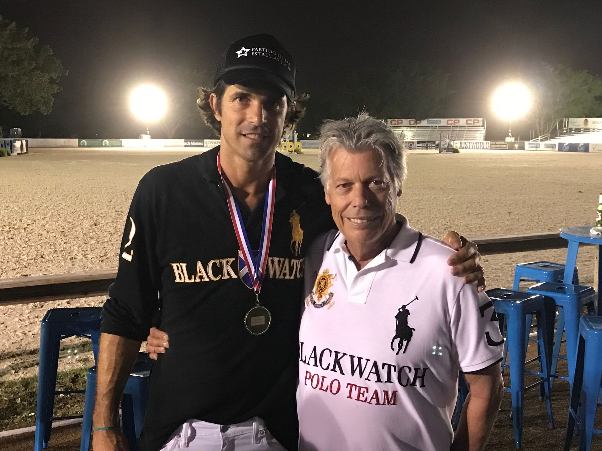 Two men posing for a picture with one wearing a black watch polo team shirt