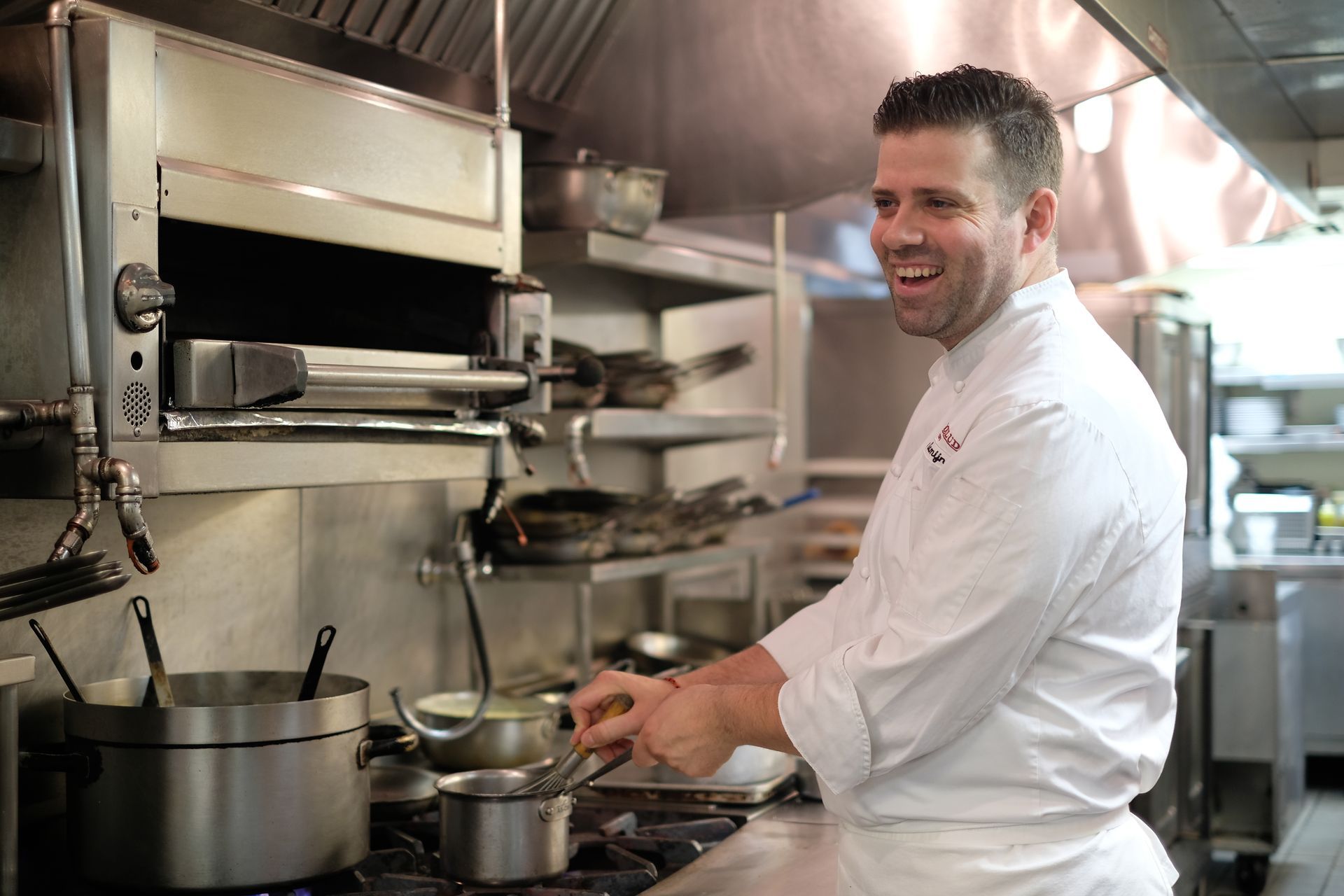 A chef is smiling while cooking in a kitchen.