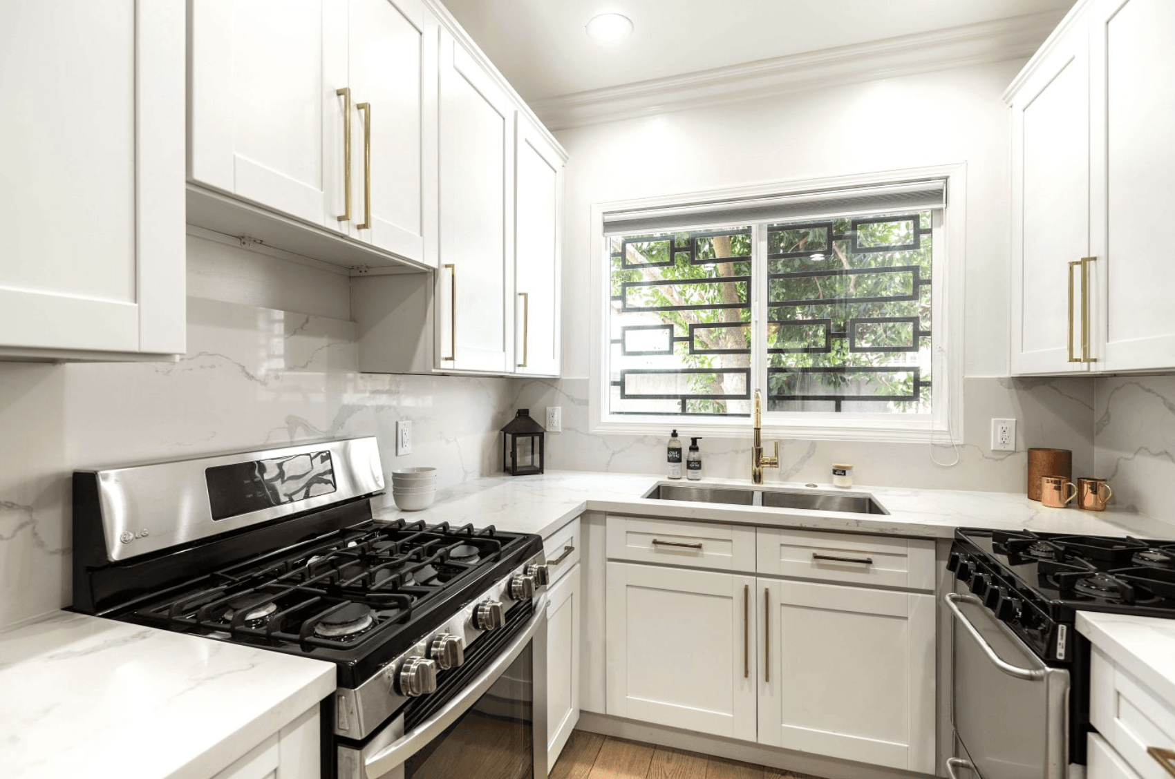 A kitchen with white cabinets , a stove , a sink , and a window.