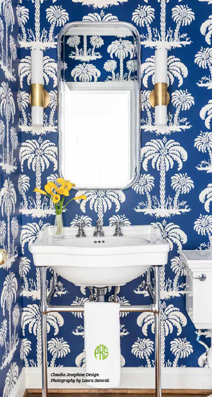 A bathroom with a sink , toilet , mirror and blue and white wallpaper.