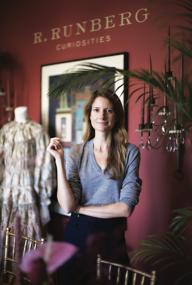 A woman is standing in front of a red wall that says r. runberg curiosities