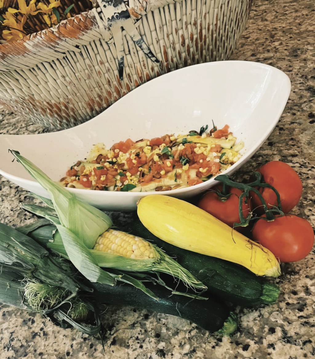 A bowl of food surrounded by vegetables including corn zucchini and tomatoes