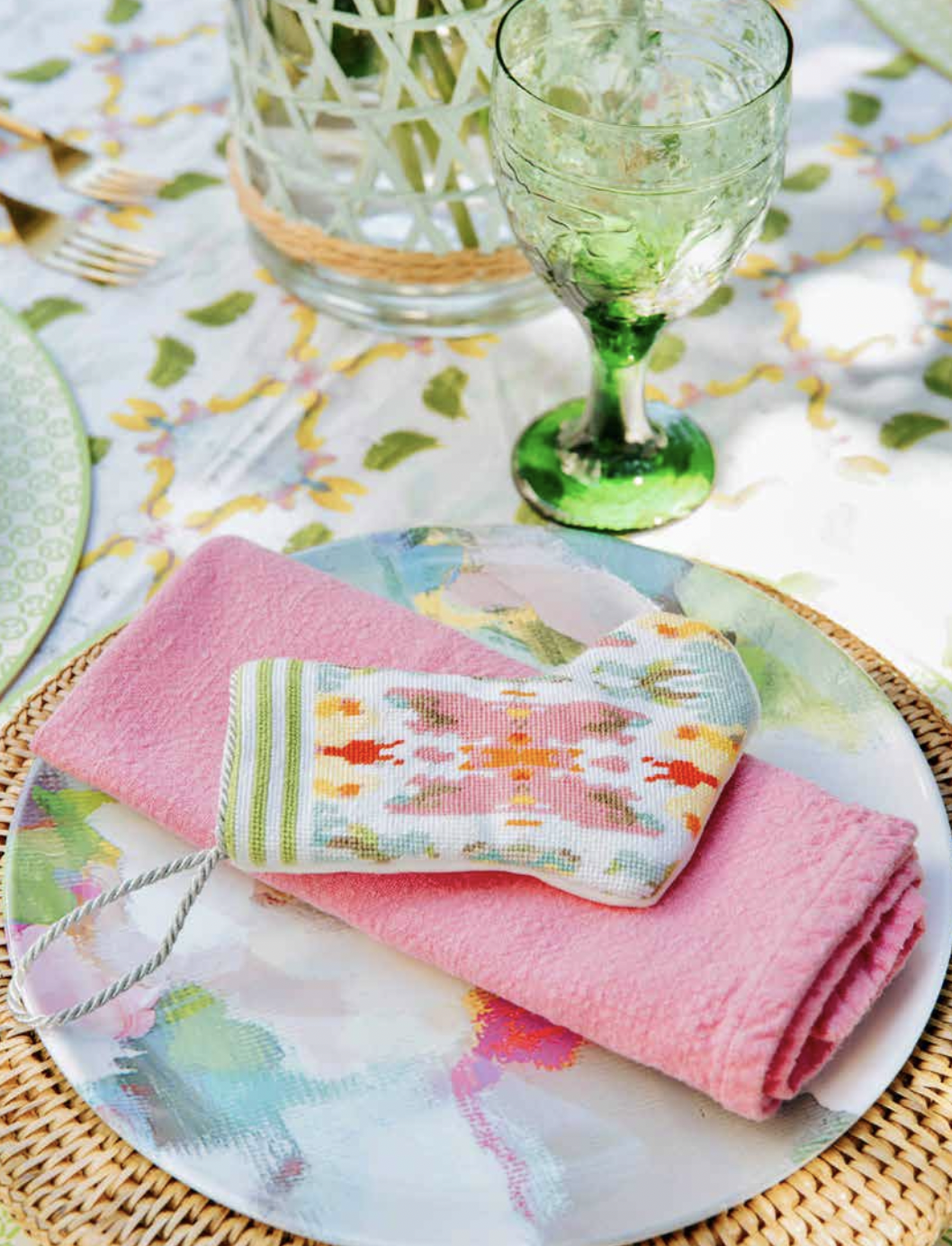 A plate with a pink napkin and a green wine glass on a table.