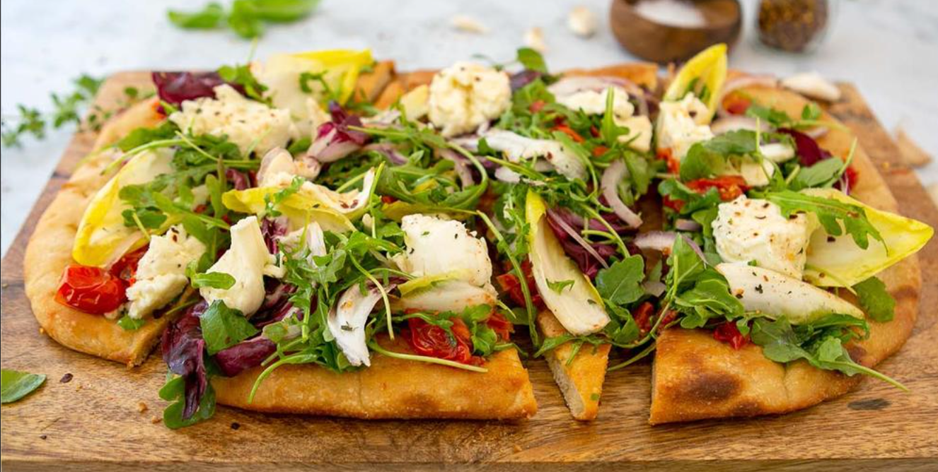 A pizza with vegetables on it is sitting on a wooden cutting board.