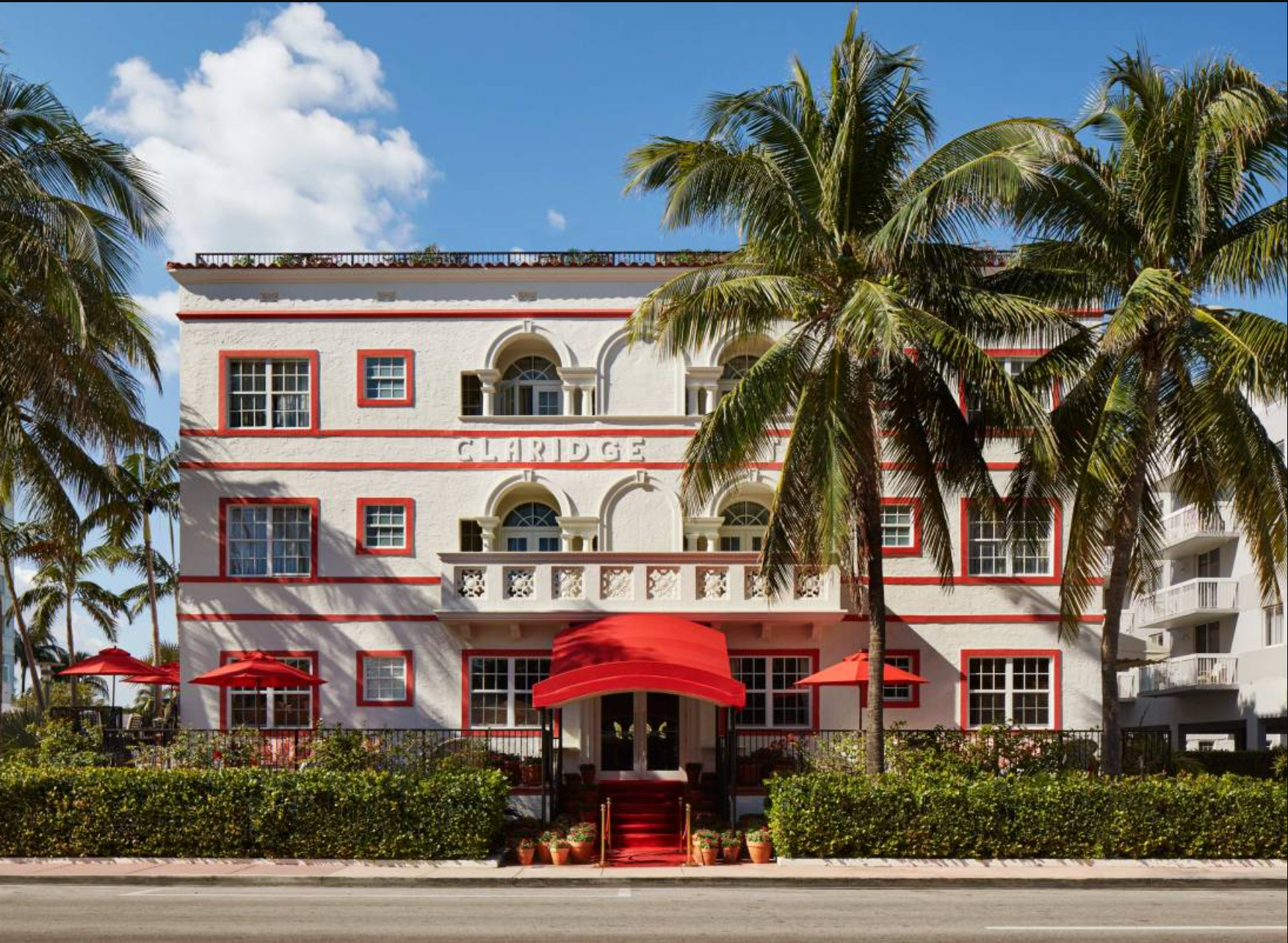 A large white building with a red awning and palm trees in front of it