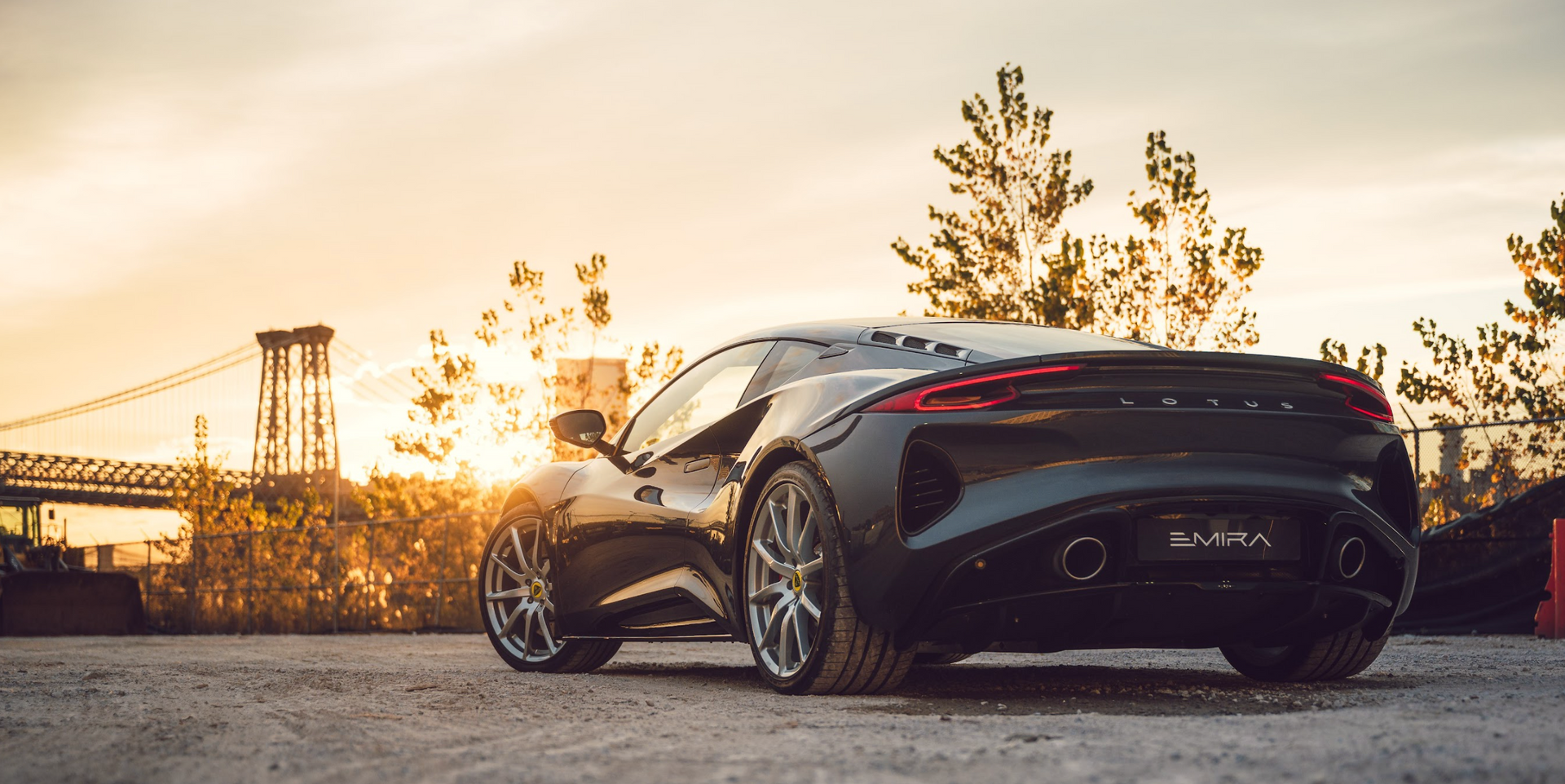 A black sports car is parked on the side of the road in front of a bridge at sunset.