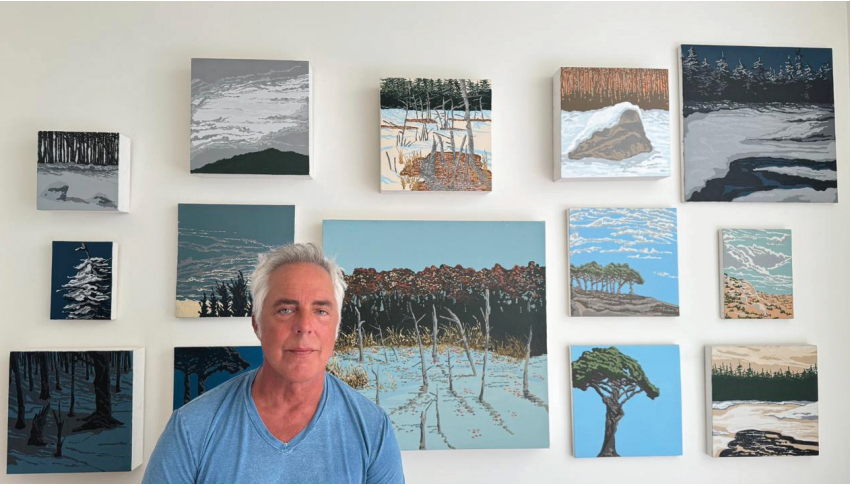 A man in a blue shirt is standing in front of a wall of paintings.