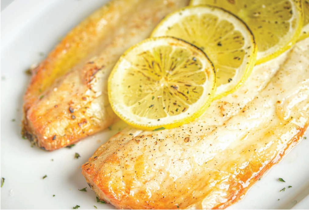 Two pieces of fish with lemon slices on a white plate.