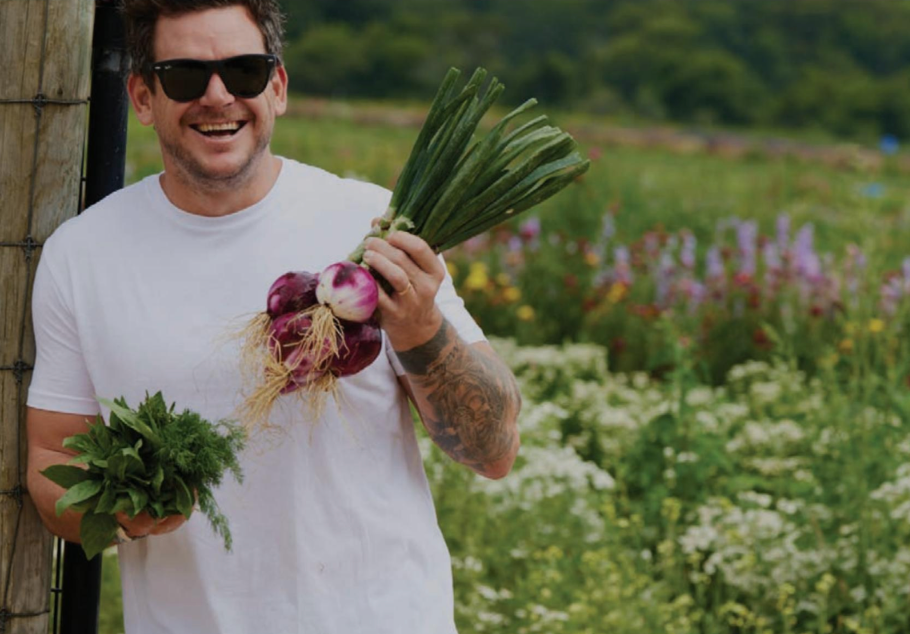 A man wearing sunglasses is holding a bunch of vegetables in a field.