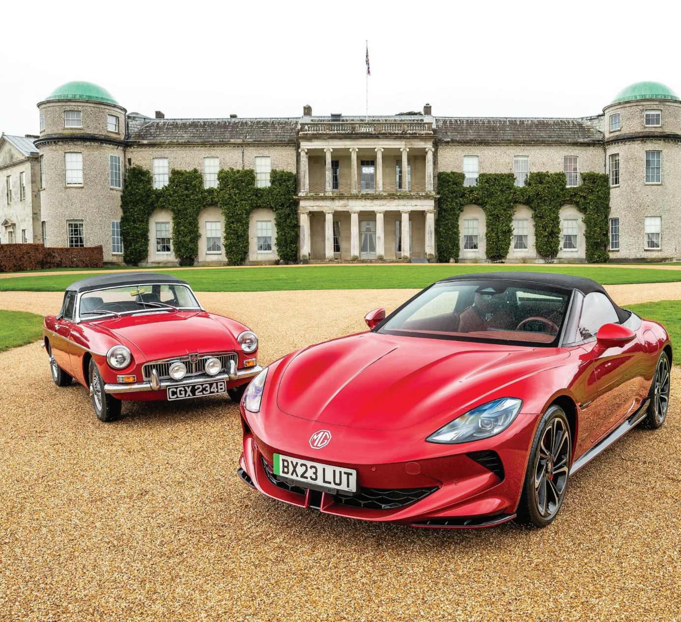 Two red sports cars are parked in front of a large building.