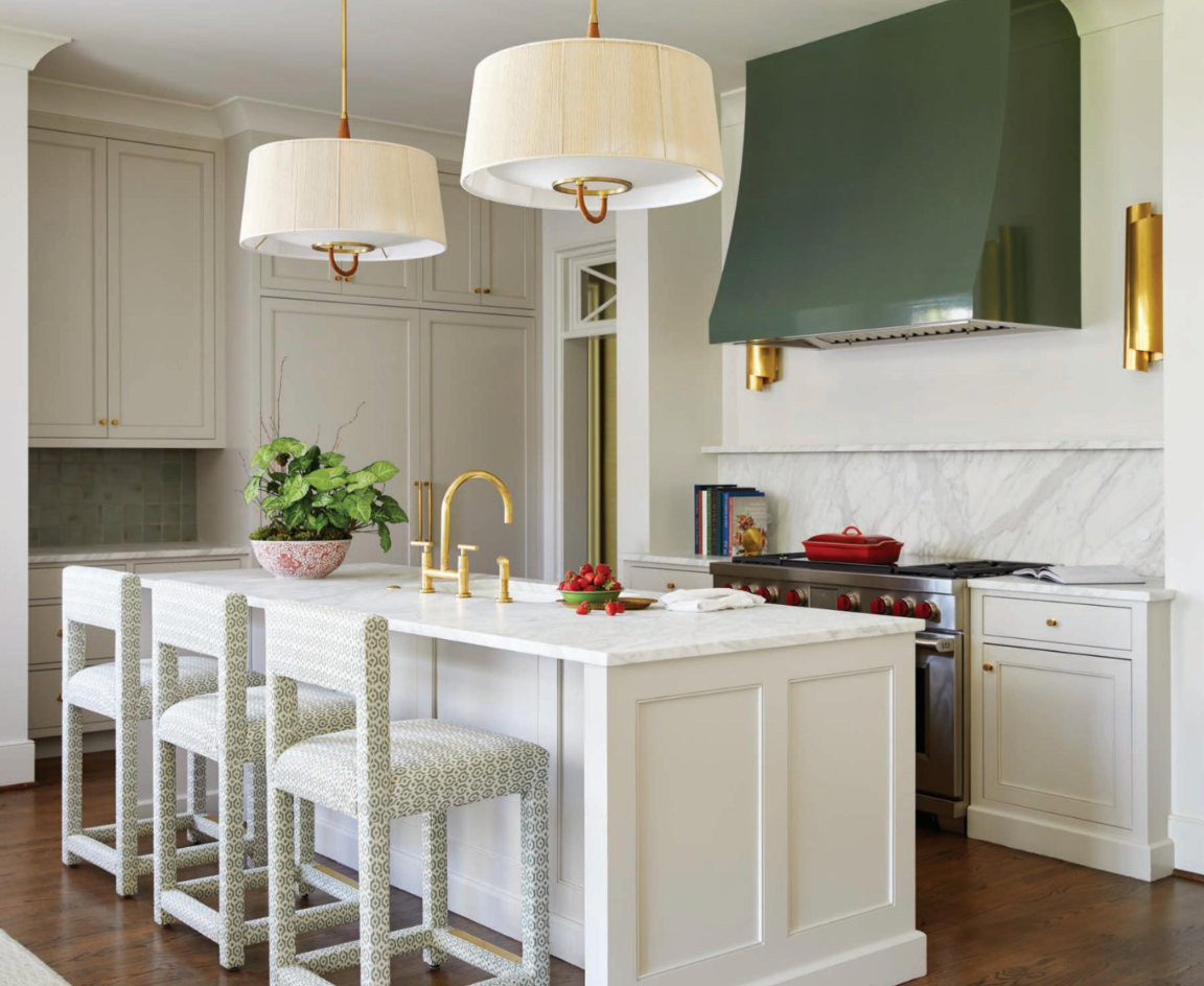 A kitchen with white cabinets , a large island , stools and a green hood.