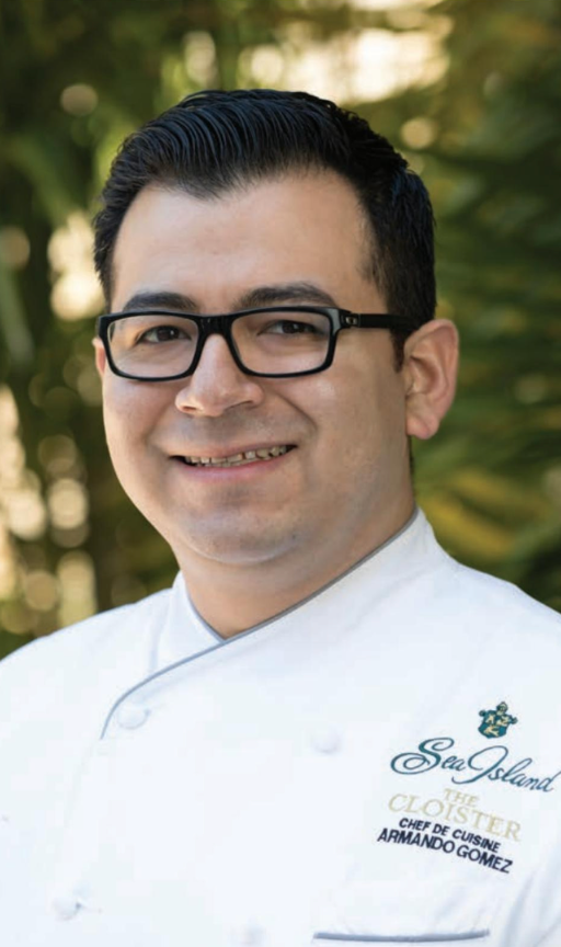 A man wearing glasses and a chef 's jacket is smiling for the camera.