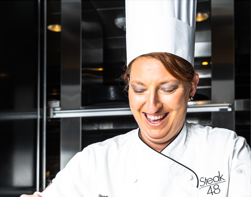 A woman in a chef 's uniform is smiling