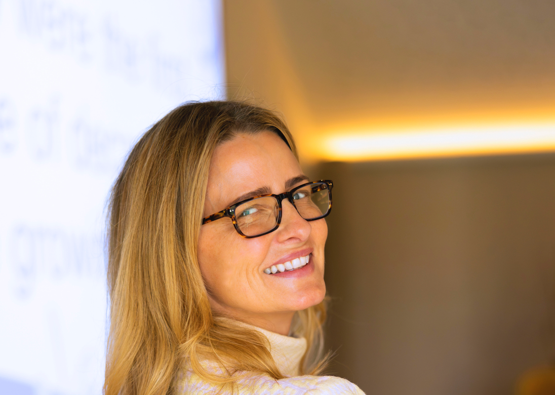 A woman wearing glasses and a white turtleneck is smiling.