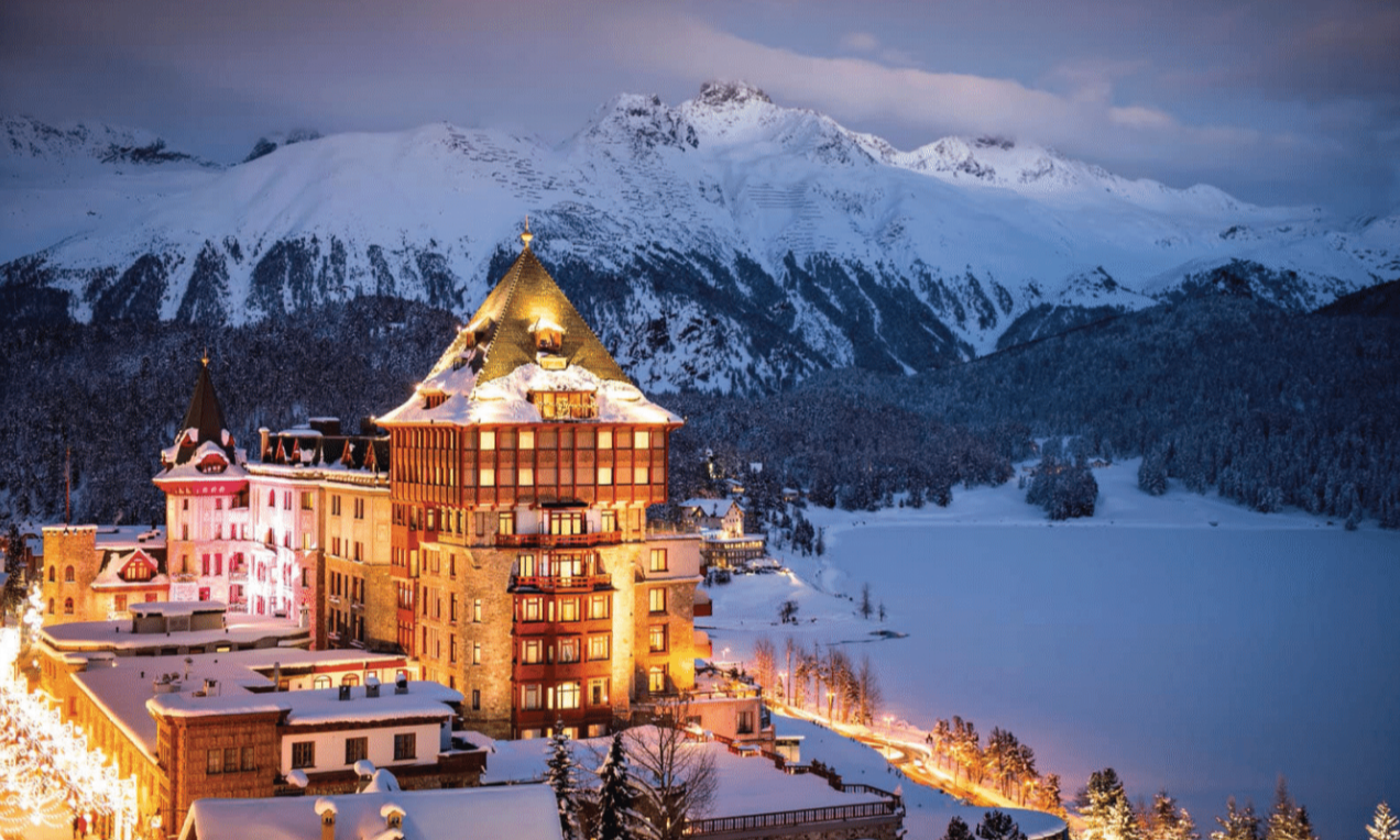 A large building is surrounded by snow covered mountains.