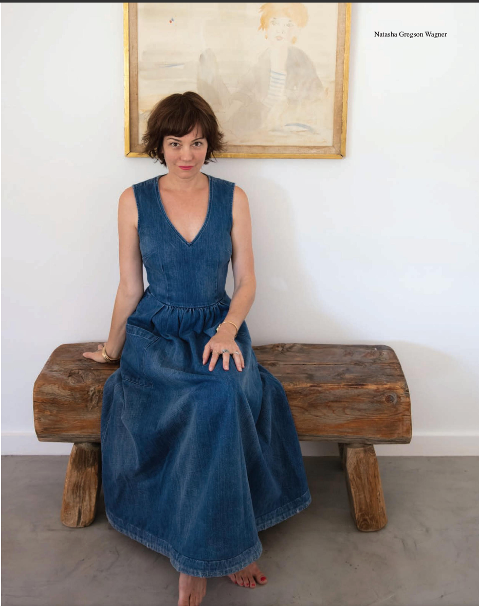 A woman in a denim dress is sitting on a wooden bench